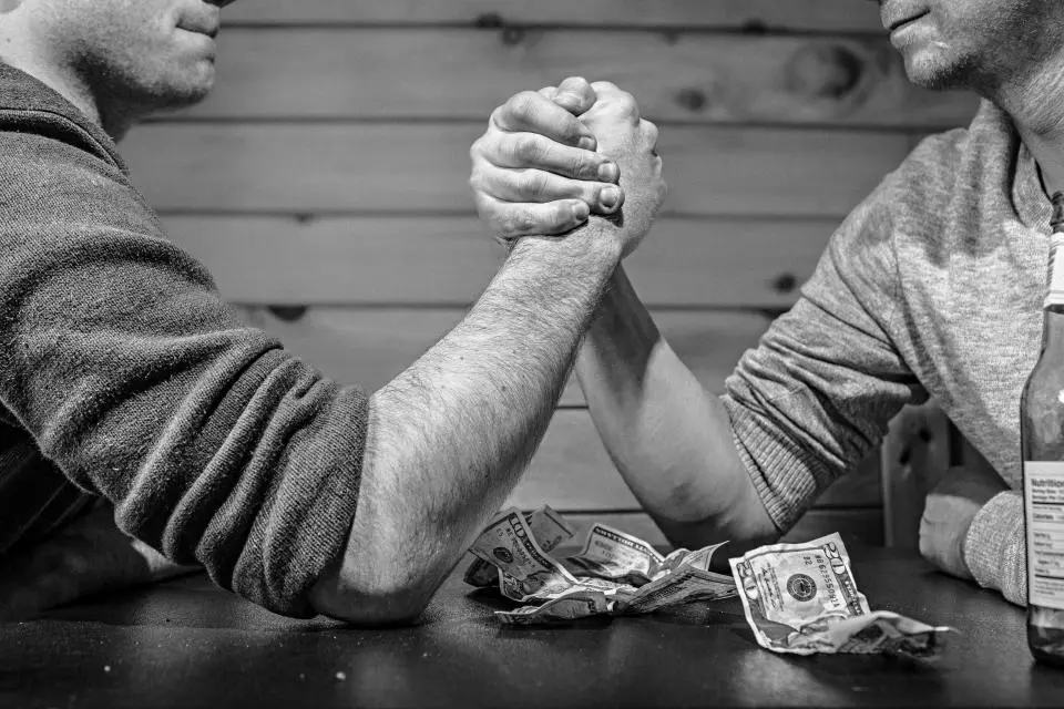 Dos personas en un pulso con billetes sobre la mesa