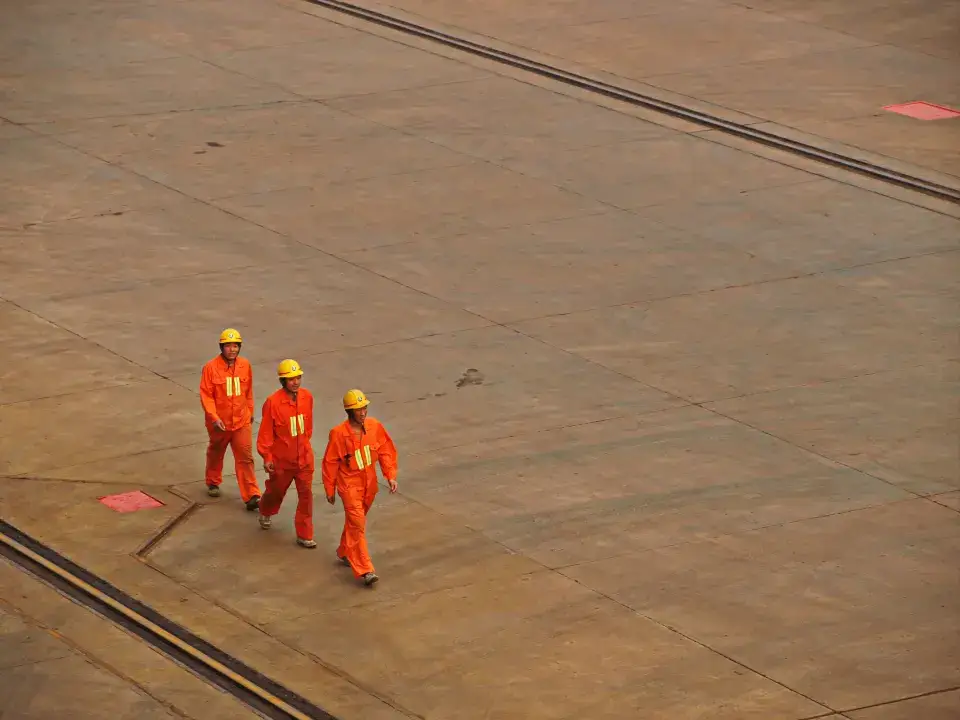 Trabajadores con casco y overol caminando en una zona industrial